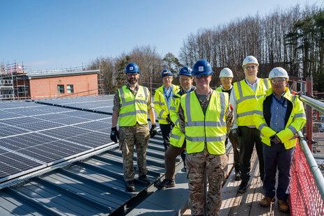 A group of people in high vis and helmets stand on a roof covered in solar panels.